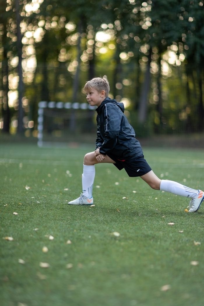 Crafting Captivating Headlines: Your awesome post title goes here Boy in sportswear stretching on a soccer field amidst lush trees, preparing for a game.