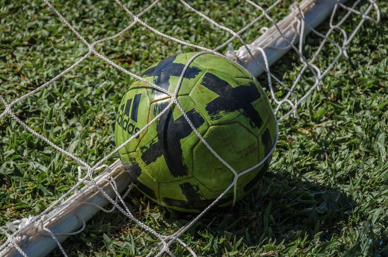 Services Bright green soccer ball stuck in a net on a grassy field in sunlight.
