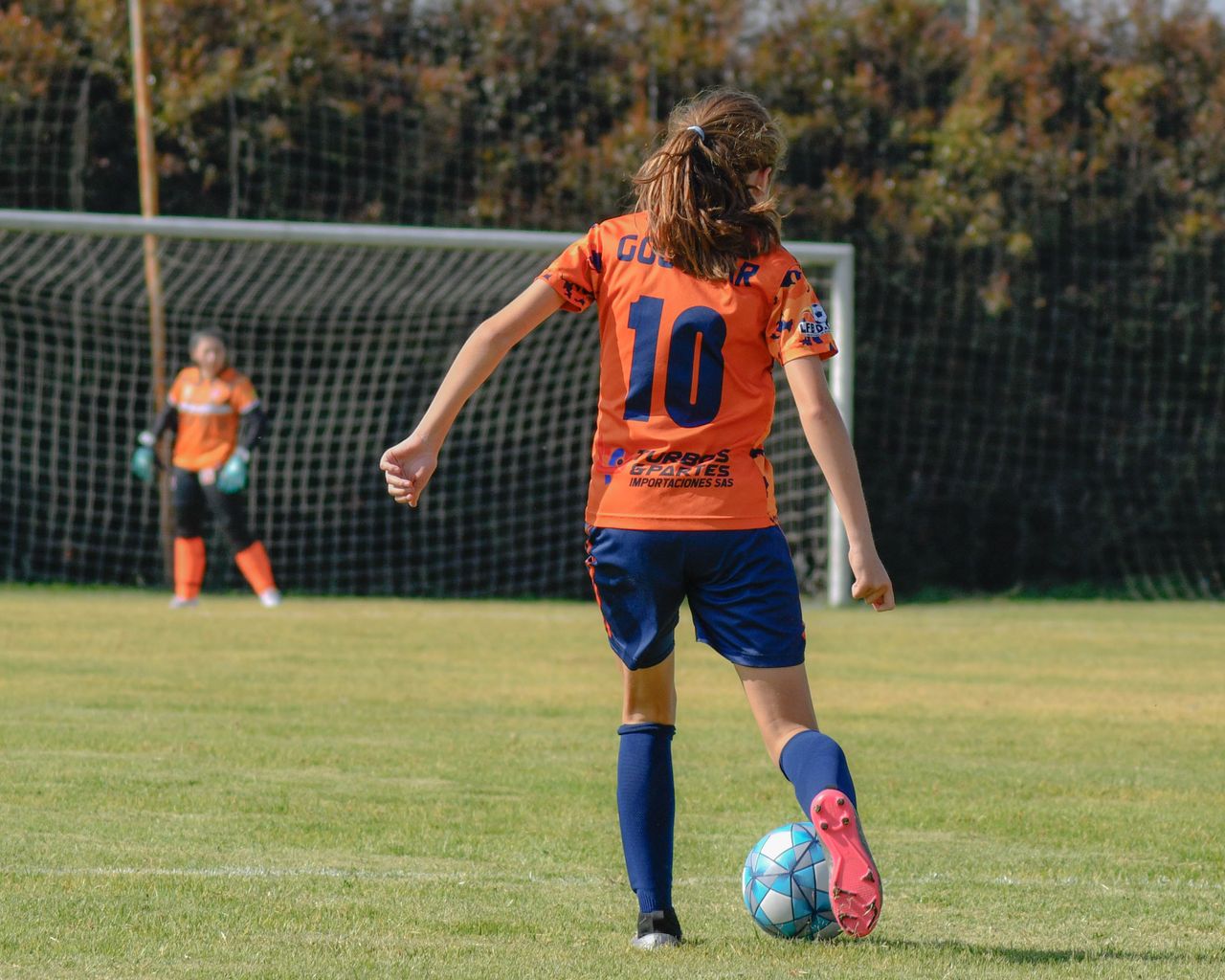 About Girl in sportswear kicking soccer ball during match on green field.