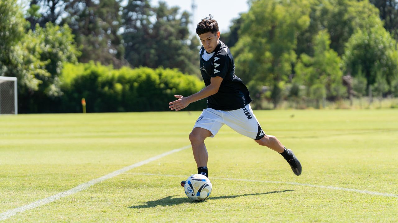 Home A teenager playing soccer on a sunny day, dribbling the ball on a grassy field.